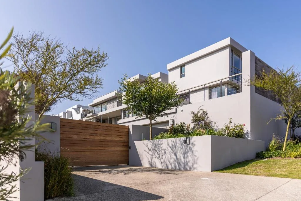 Modern white villa with wooden garage gate and manicured garden entrance