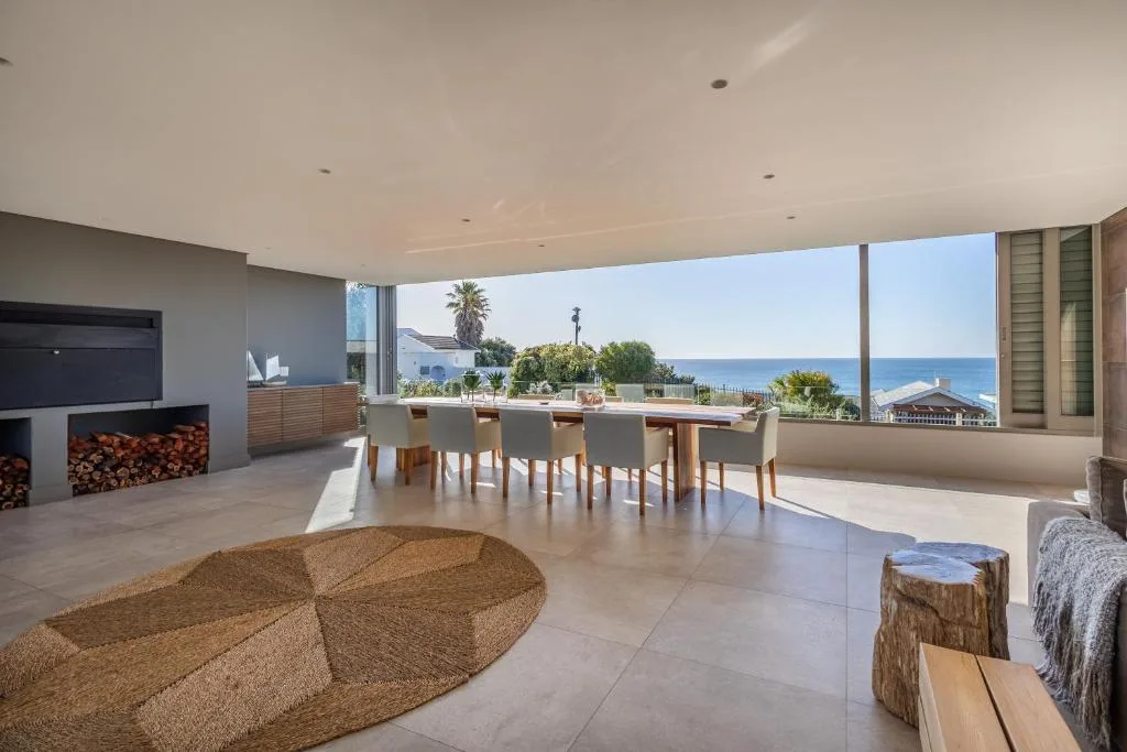 Modern lounge with fireplace overlooking ocean, dining table visible beyond