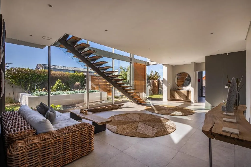 Modern lounge with wicker seating, floating staircase, and garden views