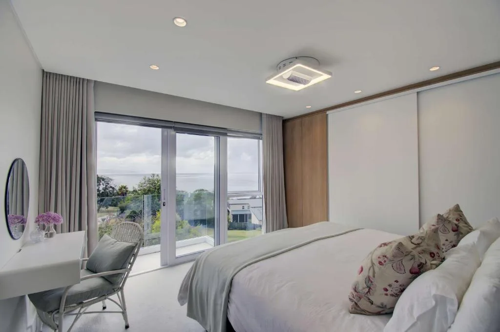 Bright bedroom with ocean views through floor-to-ceiling windows and sliding doors
