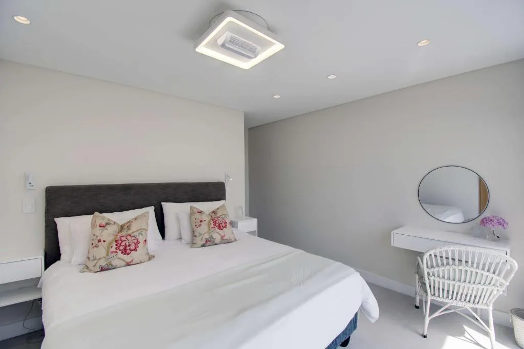 Bright modern bedroom with dark headboard bed, floral pillows, vanity mirror, and white chair