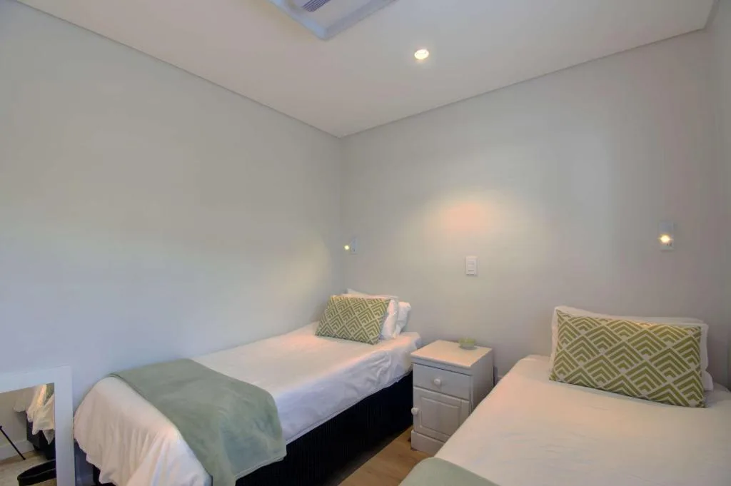 Twin bedroom with matching beds, green patterned pillows, and recessed lighting