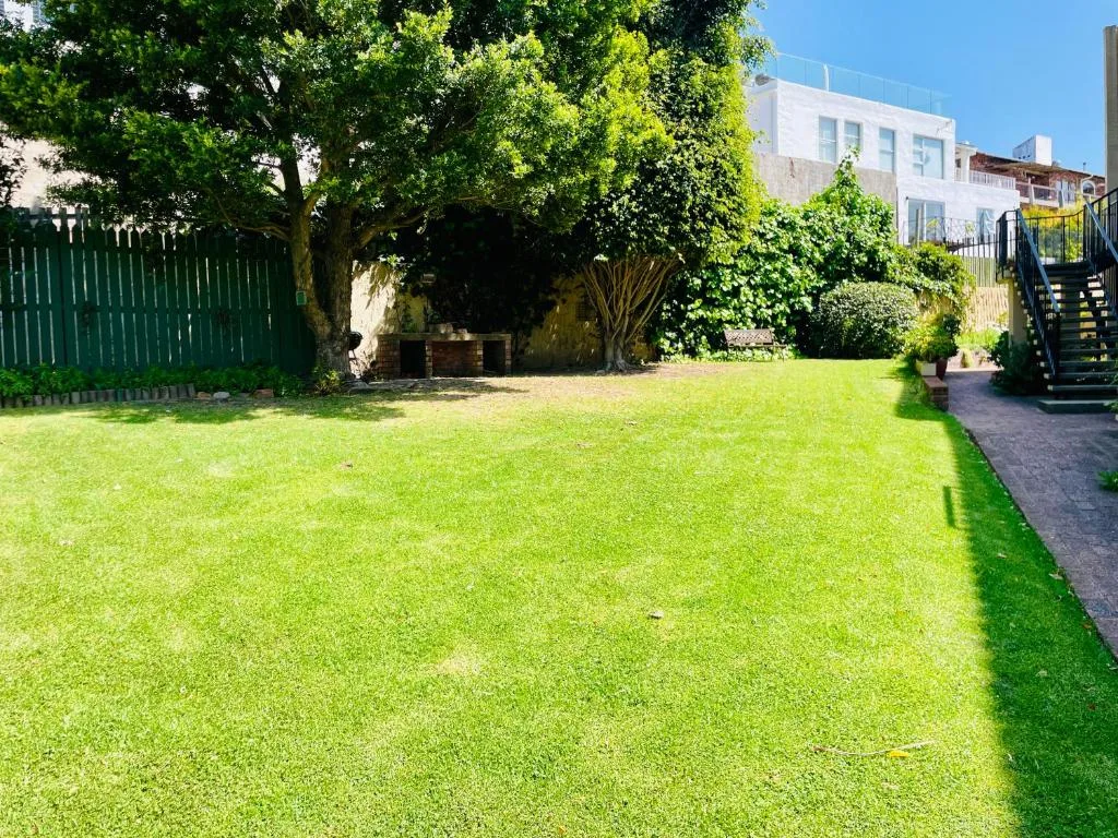Lush green lawn with mature trees and white building facade behind