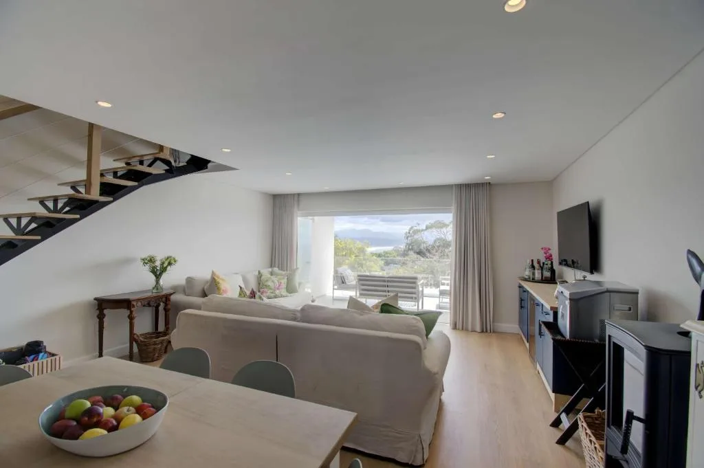 Open-plan lounge with beige sofa, TV, and scenic lagoon views through glass doors