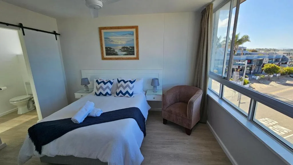 Bright bedroom with double bed, armchair, and large windows overlooking town