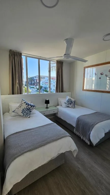 Twin bedroom with white headboards, patterned cushions, and seaside town view