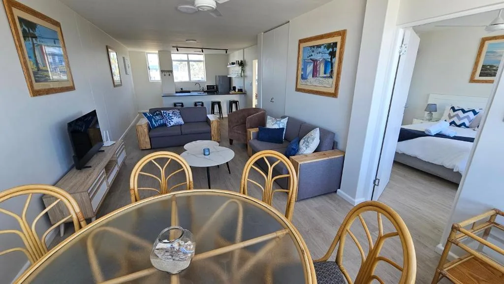 Open-plan lounge with grey sofas, TV, and dining table with rattan chairs