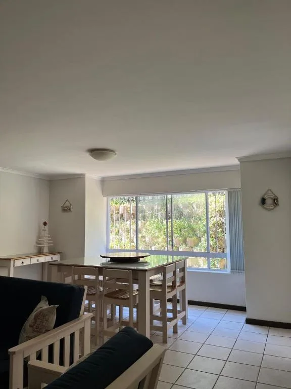 Dining area with wooden table, chairs, and large windows overlooking garden
