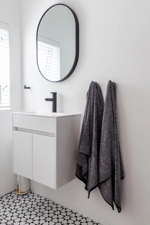 Modern bathroom vanity with oval mirror and dark towels hanging