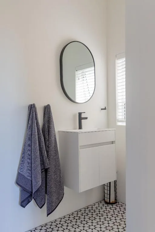 Modern bathroom vanity with oval mirror and grey towels hanging nearby