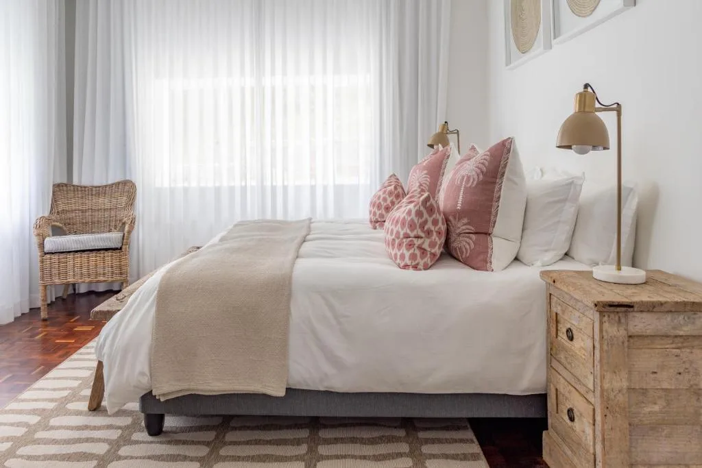 Bright bedroom with white linens, pink decorative pillows, wooden nightstand