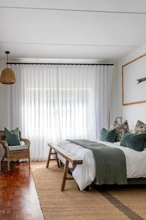 Bright bedroom with bed, wicker chair, and natural light from large windows
