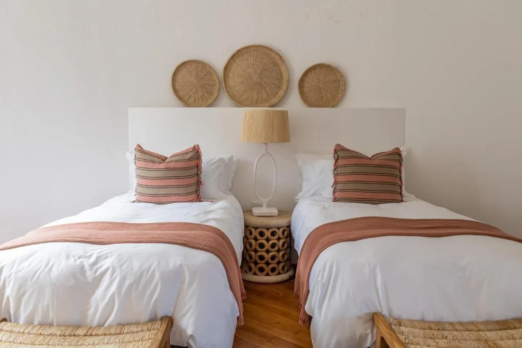 Twin beds with white bedding, striped pillows, and woven wall decor above headboard