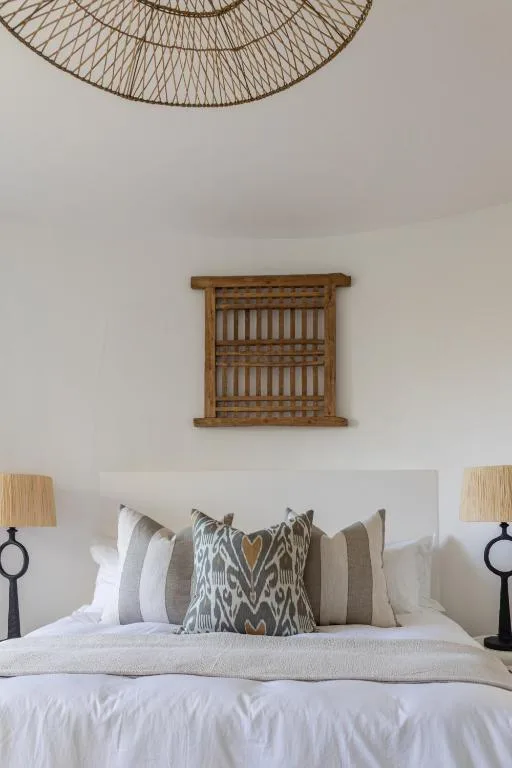 Bed with decorative pillows and woven wall hanging above headboard