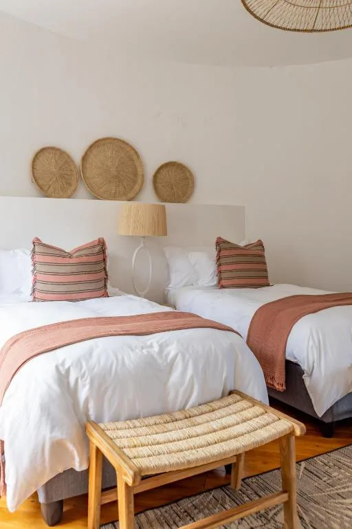 Twin beds with white linens, striped pillows, and woven wall decor above