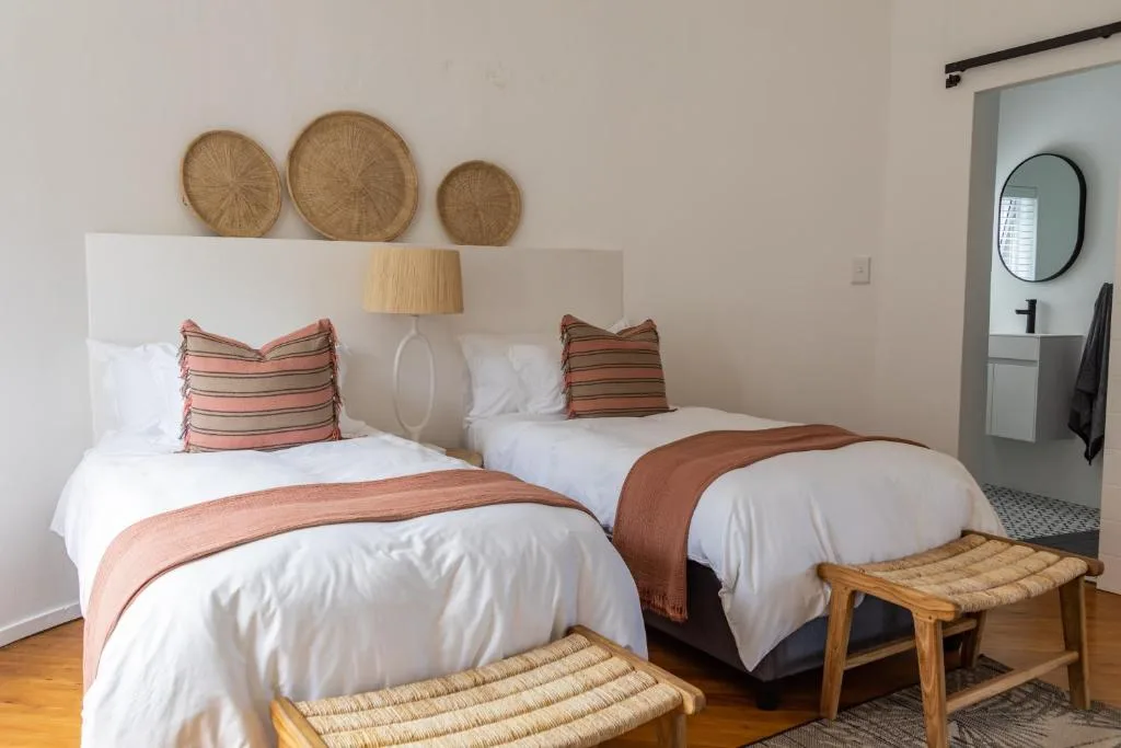 Twin beds with striped pillows, woven wall baskets, and wooden stools