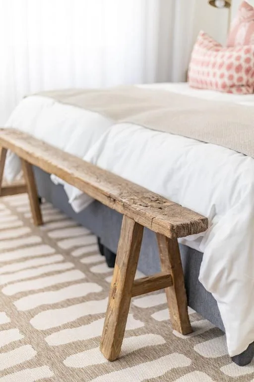 Rustic wooden bench at foot of bed with white linens and pink cushion