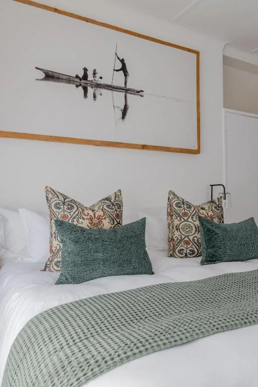Bedroom with white linens, decorative pillows, and framed boat artwork