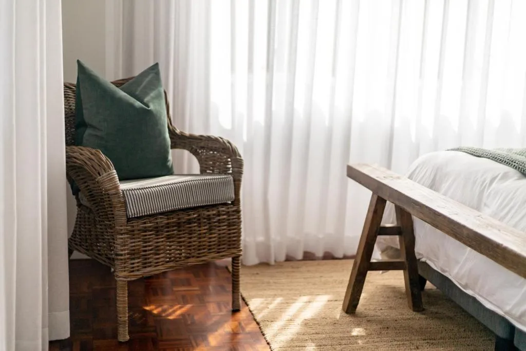 Bright bedroom with wicker chair, green pillow, and wooden bed frame