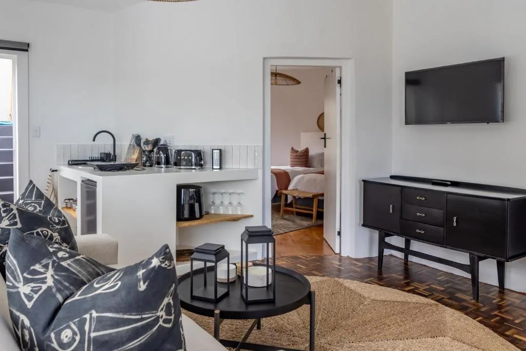 Open-plan lounge with sofa, TV, kitchenette, and bedroom view beyond