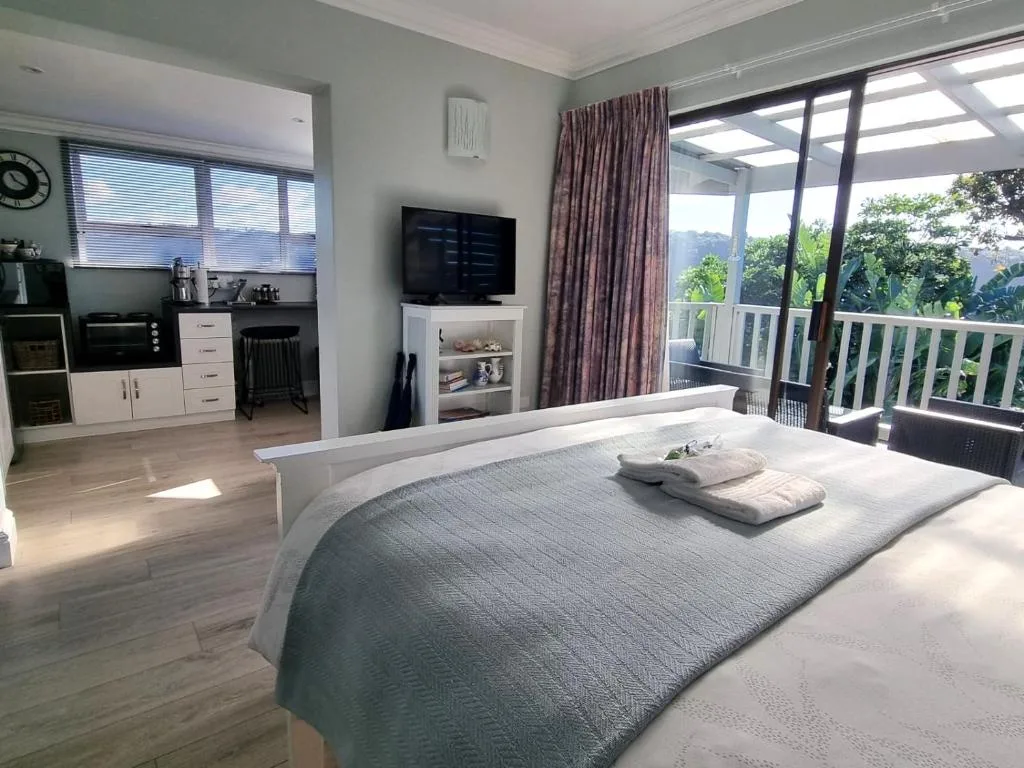 Bright bedroom with queen bed, TV, and panoramic deck overlooking lush garden views