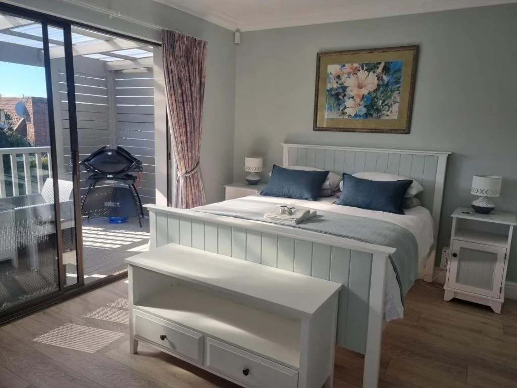 Bright bedroom with white bed, blue pillows, and deck access overlooking views