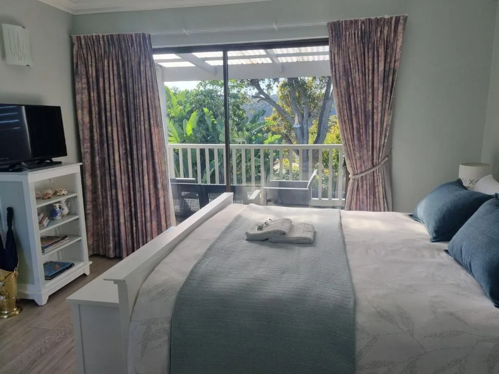 Bright bedroom with queen bed, balcony doors overlooking trees and garden