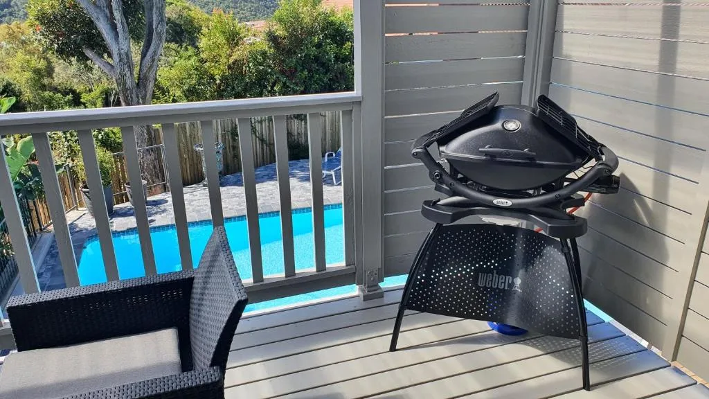 Outdoor deck with Weber braai, seating, and pool views beyond railing