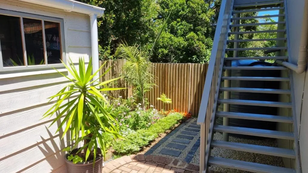 Modern apartment exterior with lush garden, stairs, and tropical plants