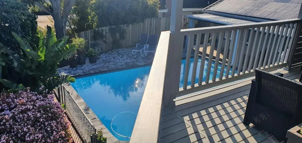Swimming pool viewed from elevated deck with flowering garden and lounge chairs