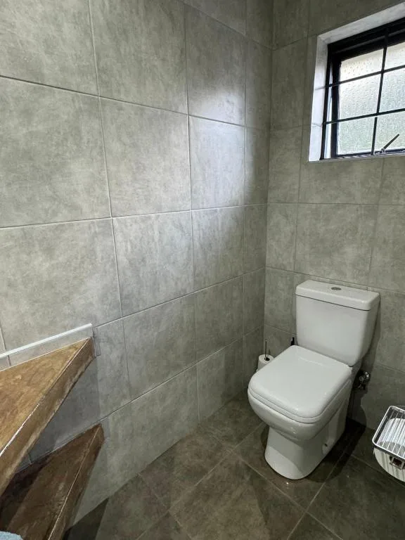 Modern bathroom with grey tile walls, white toilet, and small window