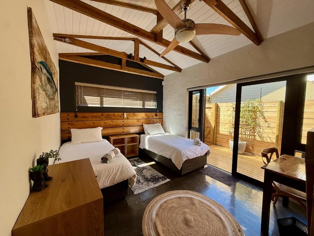 Twin bedroom with wooden headboard, vaulted timber ceiling, and deck access