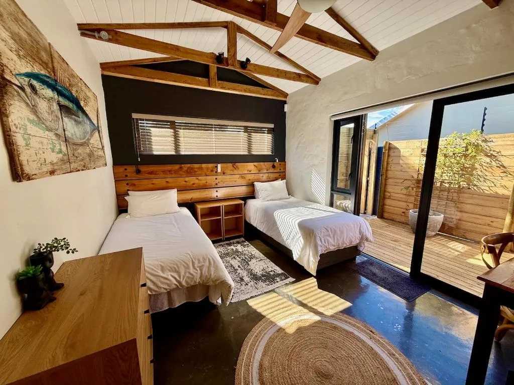 Bright bedroom with two single beds, wooden beams, and glass doors to patio
