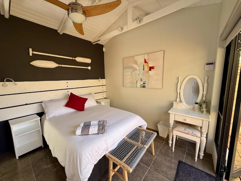 Bright bedroom with queen bed, white headboard, ceiling fan, vanity mirror