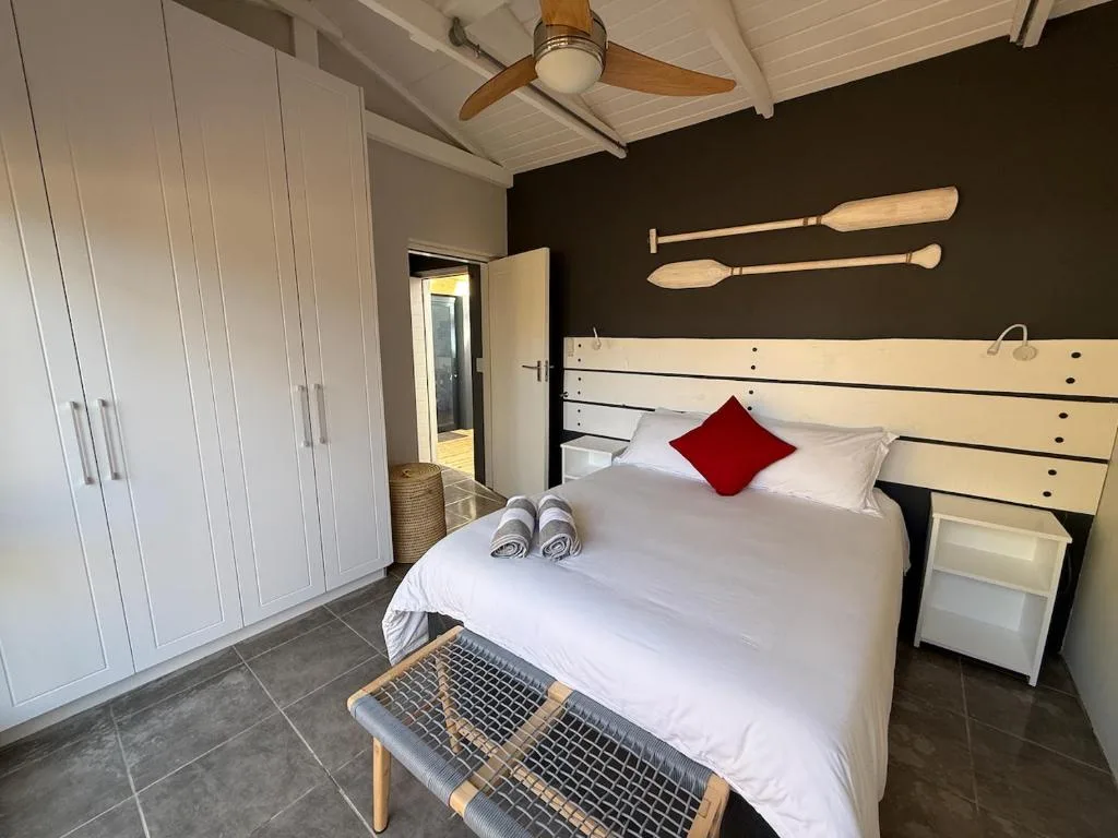 Modern bedroom with white bed, red pillow, wooden ceiling fan, dark accent wall