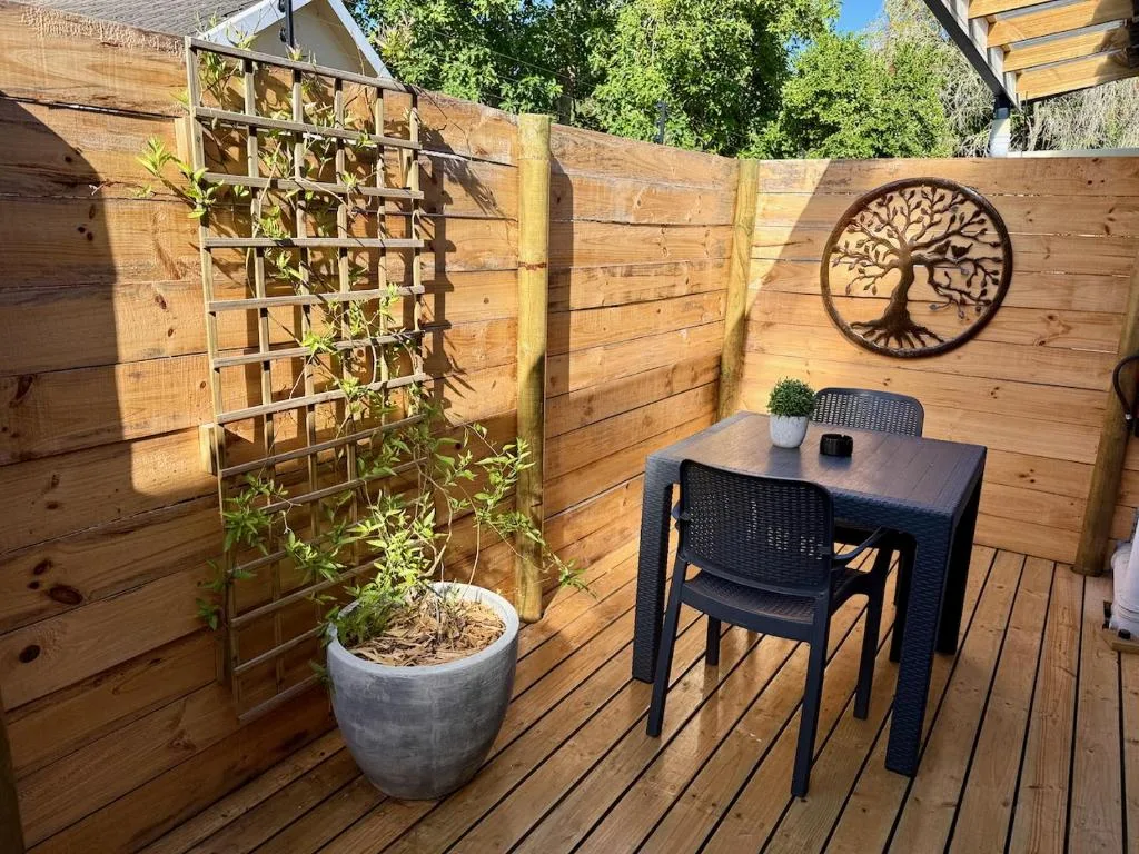 Wooden deck with outdoor dining table, potted plant, and tree wall art