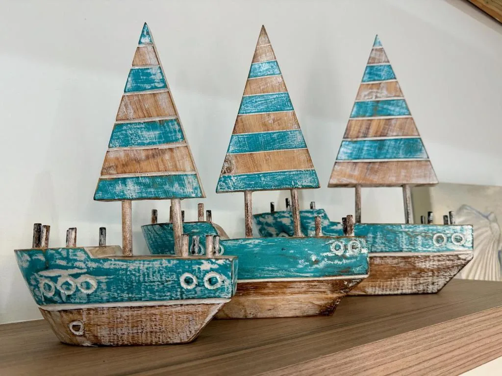 Three decorative wooden boats with turquoise sails on wooden shelf