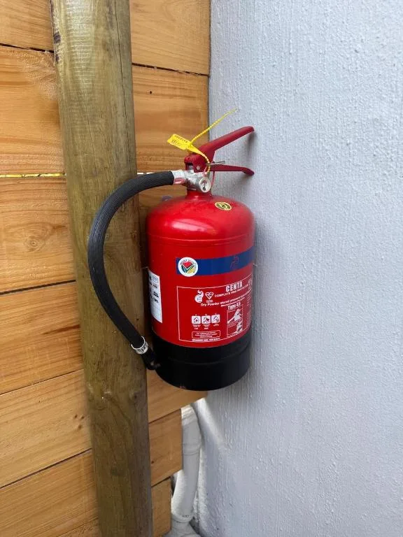 Red fire extinguisher mounted on wall between wooden post and white plaster