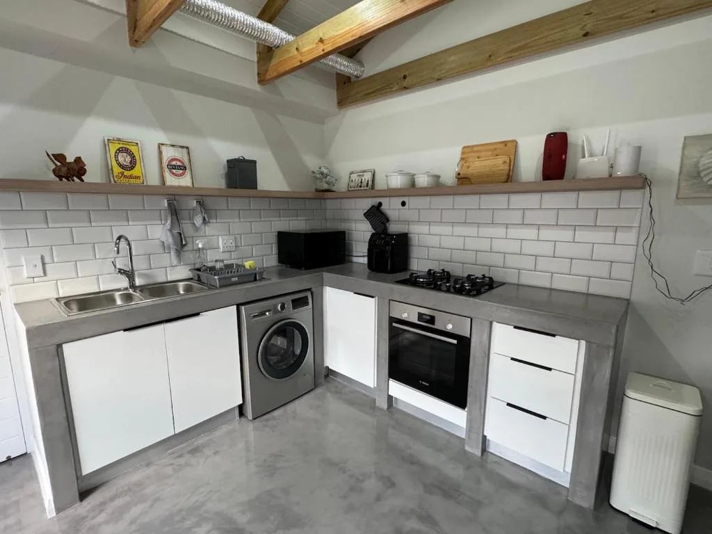 Modern kitchen with white cabinetry, stainless steel counters, and exposed wooden beams