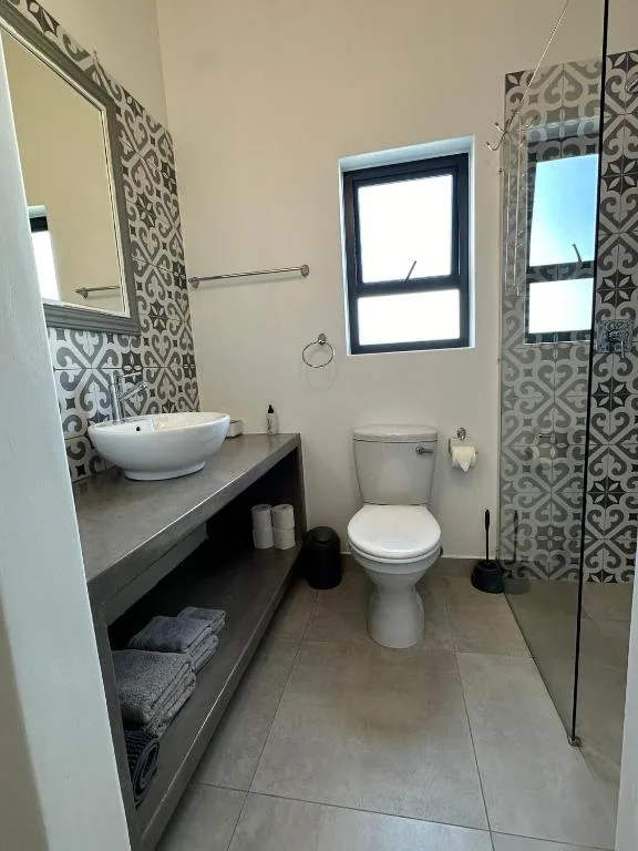 Modern bathroom with vessel sink, toilet, patterned tiles, and shower enclosure