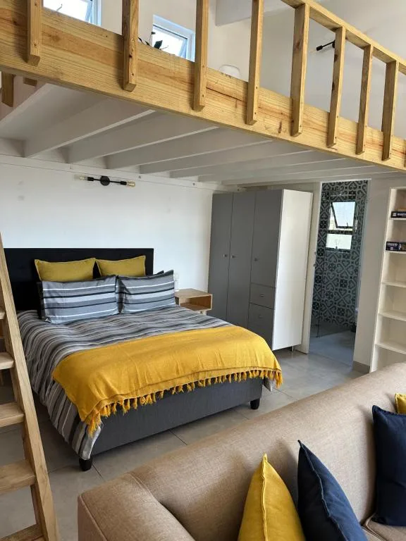 Modern bedroom with queen bed, yellow bedding, wooden loft above, and gray wardrobe