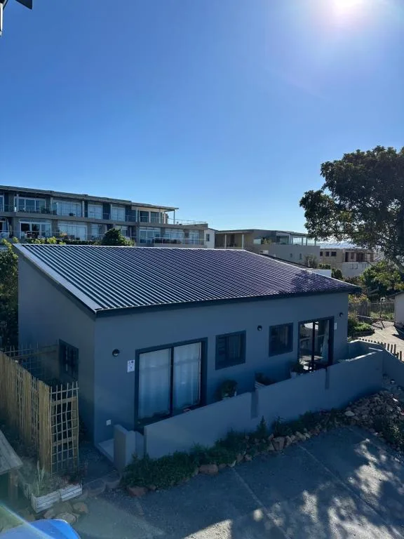 Modern white building with dark metal roof and large windows under blue sky