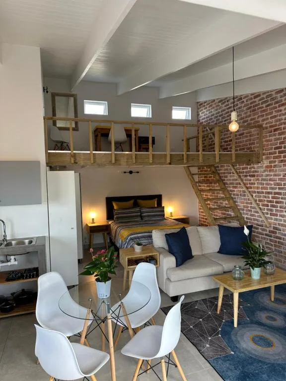 Open-plan lounge with sofa, dining chairs, and lofted bedroom above