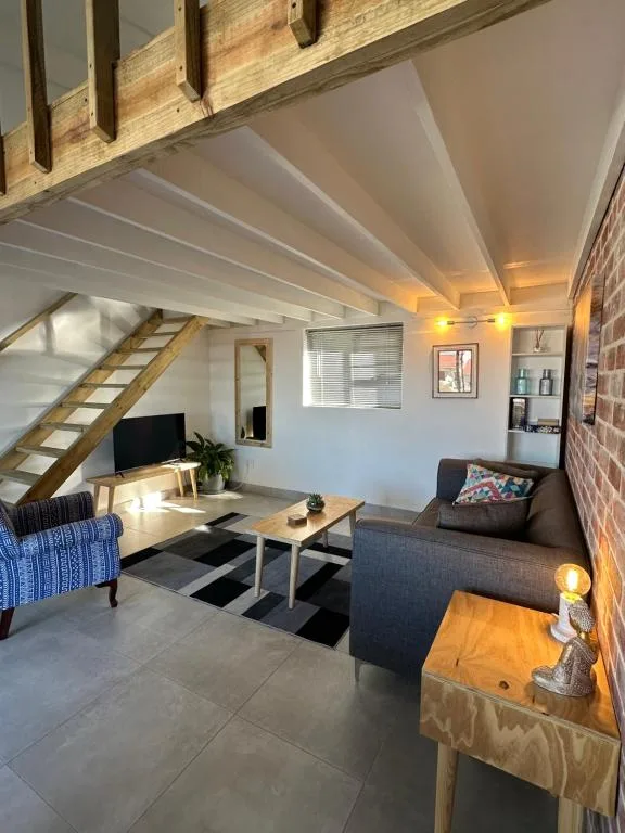 Open-plan lounge with grey sofas, wooden beams, and staircase