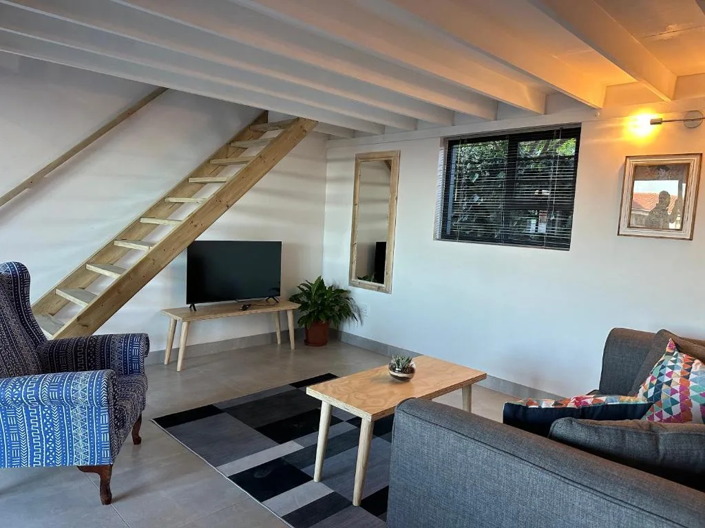 Open-plan lounge with sofa, TV, wooden stairs, and natural light