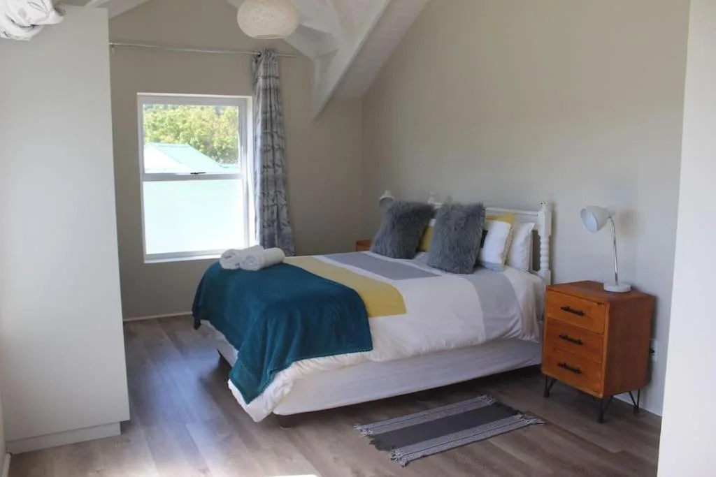 Bright bedroom with queen bed, wooden nightstand, and large window overlooking gardens