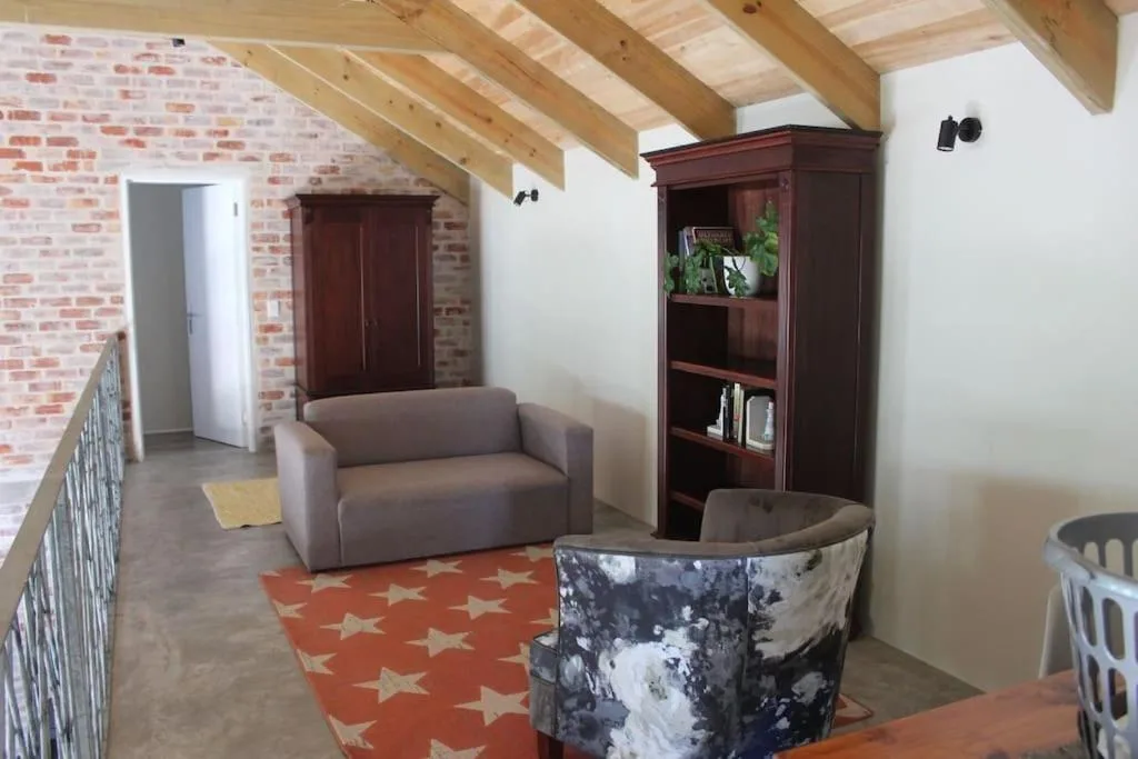 Spacious loft lounge with exposed beams, brick wall, gray sofa, and wooden shelving