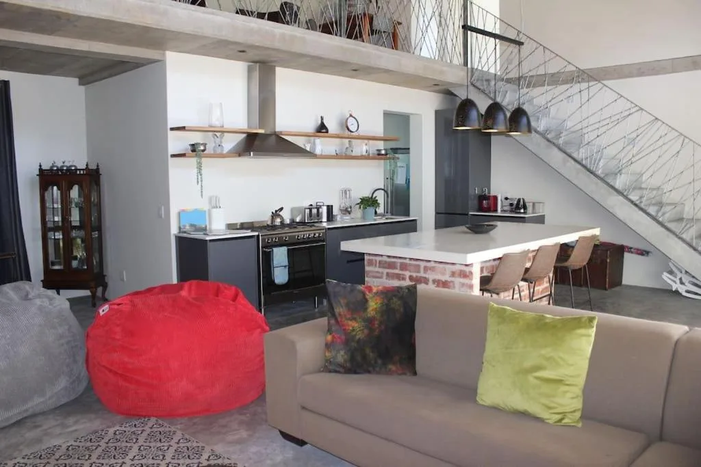 Open-plan lounge with beige sofa, red bean bag, and modern staircase