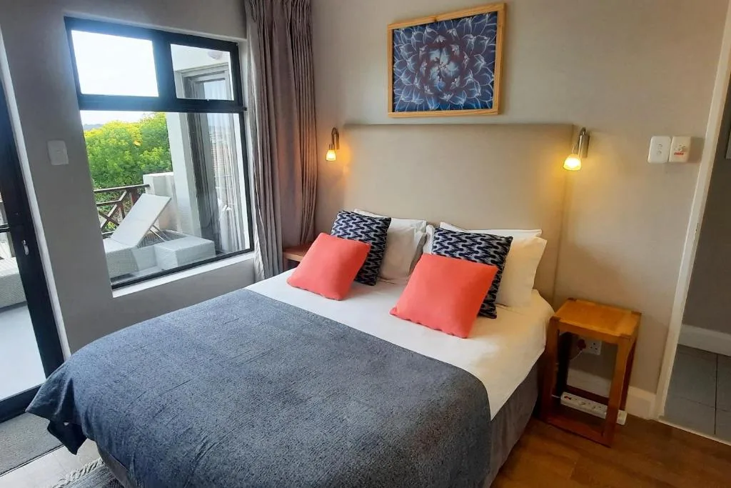 Bright bedroom with double bed, coral pillows, and garden view through sliding doors