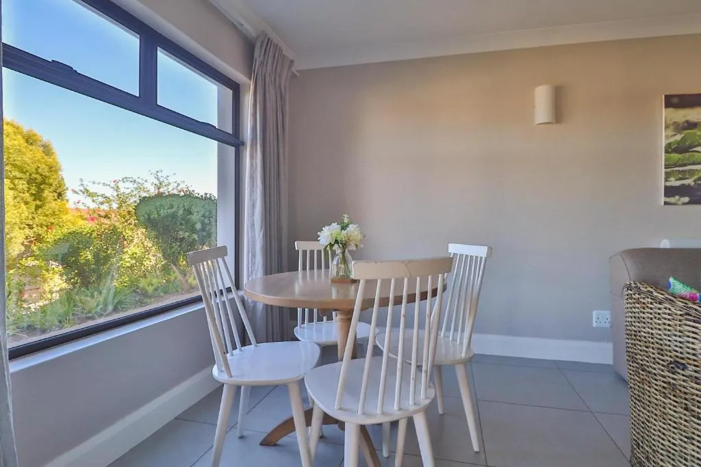 Bright dining area with wooden table, white chairs, and garden views through large windows